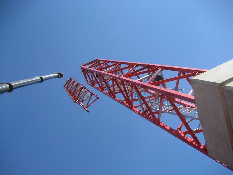 Red tower crane being assembled against a blue sky.