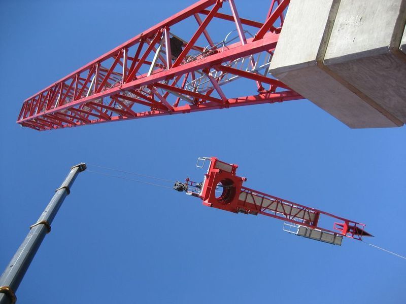 Red crane parts against a bright blue sky during construction.