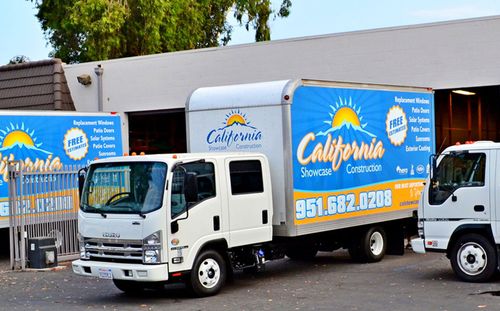 White box trucks with blue California moving company graphics parked outside a building.