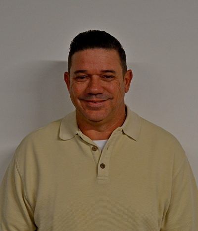 Man smiling in a beige polo shirt against a plain gray background