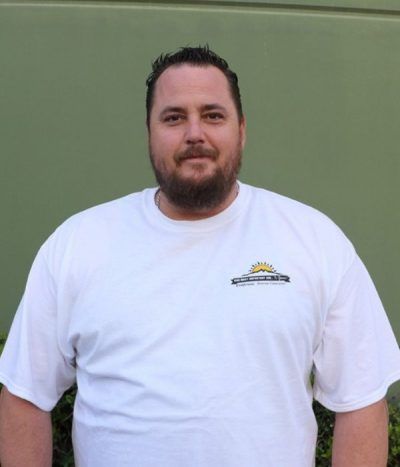 Man standing against a green wall, wearing a white T-shirt and looking at the camera.