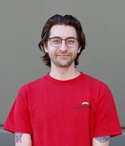 Person wearing glasses and a red T-shirt, standing against a gray background.