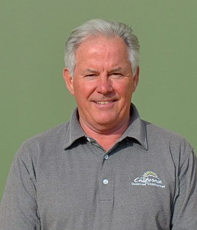 Smiling man in a gray polo shirt standing against a plain green background