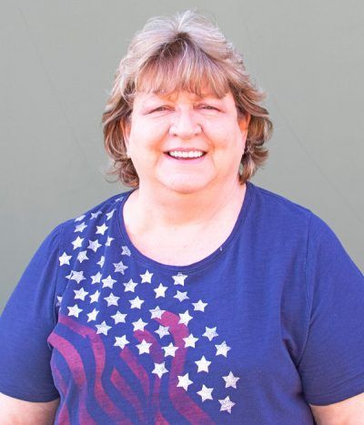 Smiling person in a blue shirt with a star-spangled American flag design against a gray background