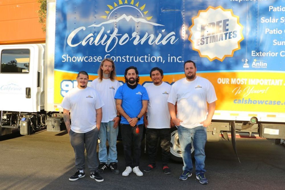 Four men posing in front of a California Showcase Construction trailer with blue and orange branding.