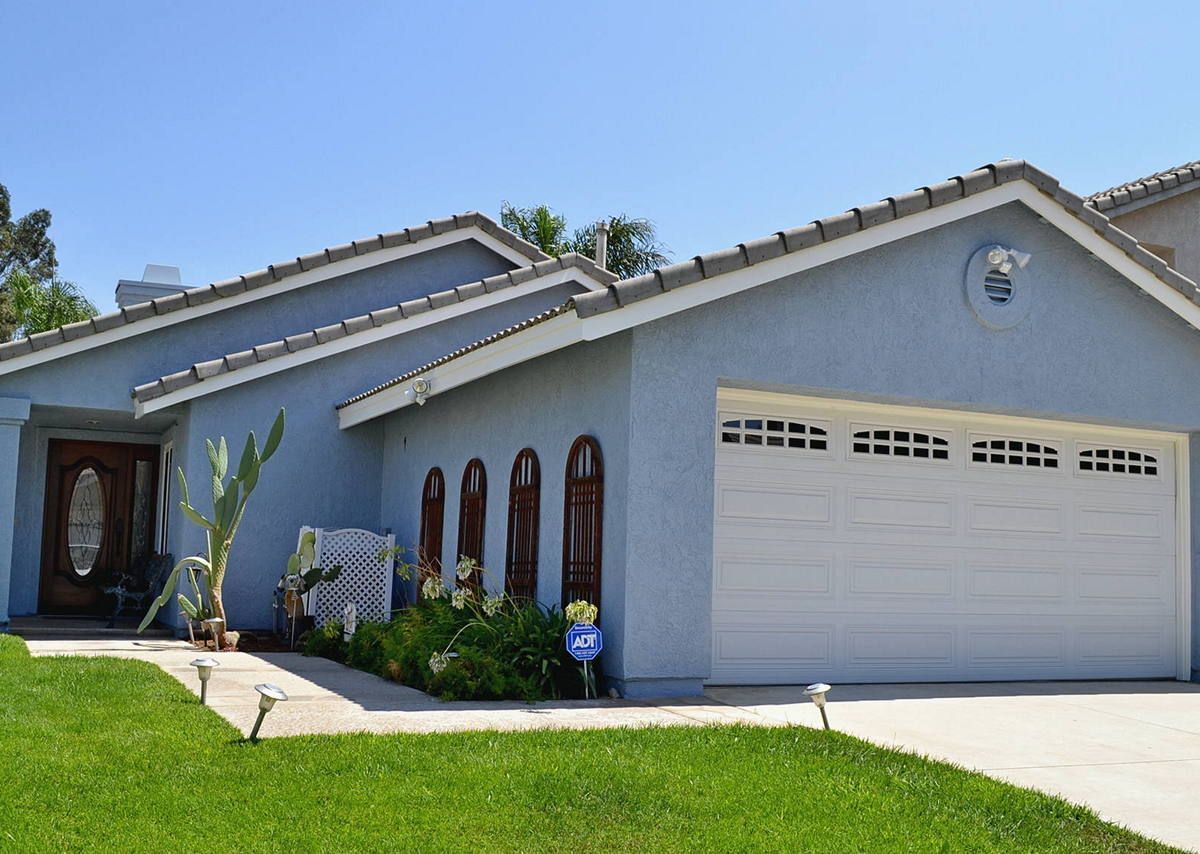 Suburban house exterior with gray stucco, white garage door, and green lawn on a sunny day