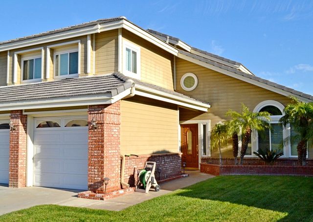 Two-story suburban house with beige siding, brick accents, garage, and a green lawn