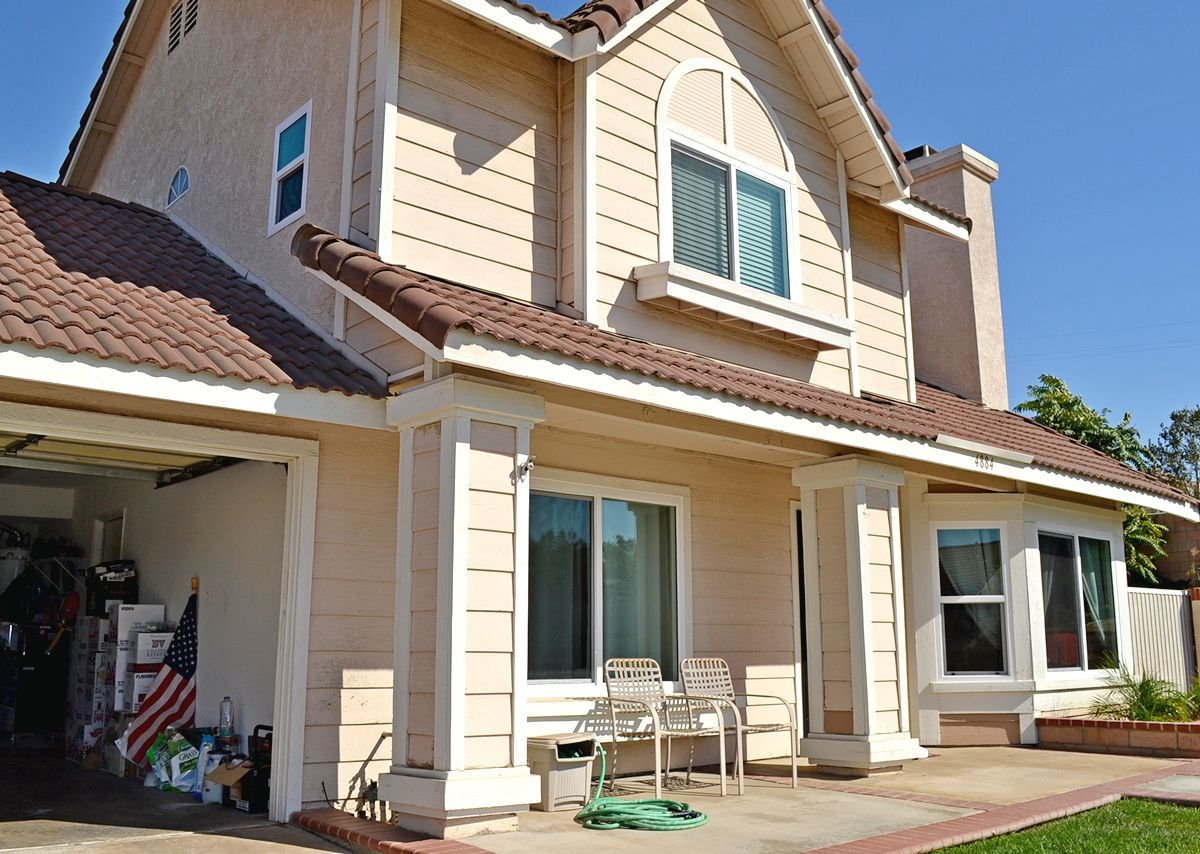 Suburban two-story beige house with a garage, front patio, and green lawn under a blue sky