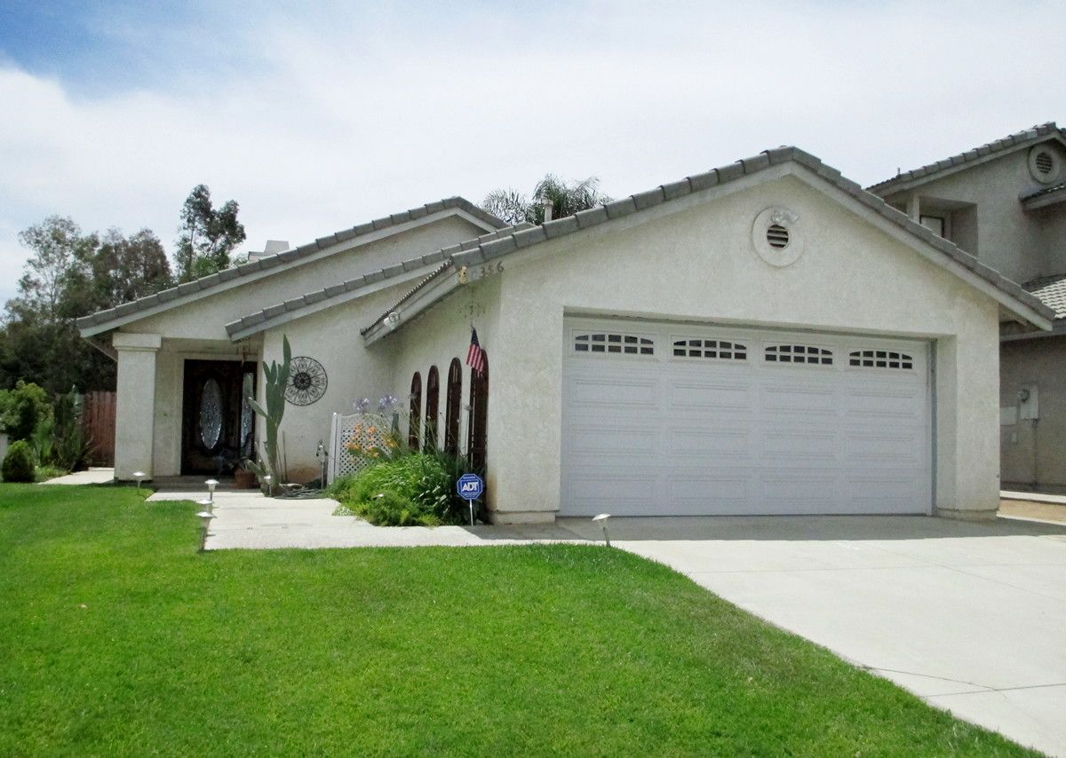Suburban single-story house with a white garage, front lawn, and palm trees by the entrance