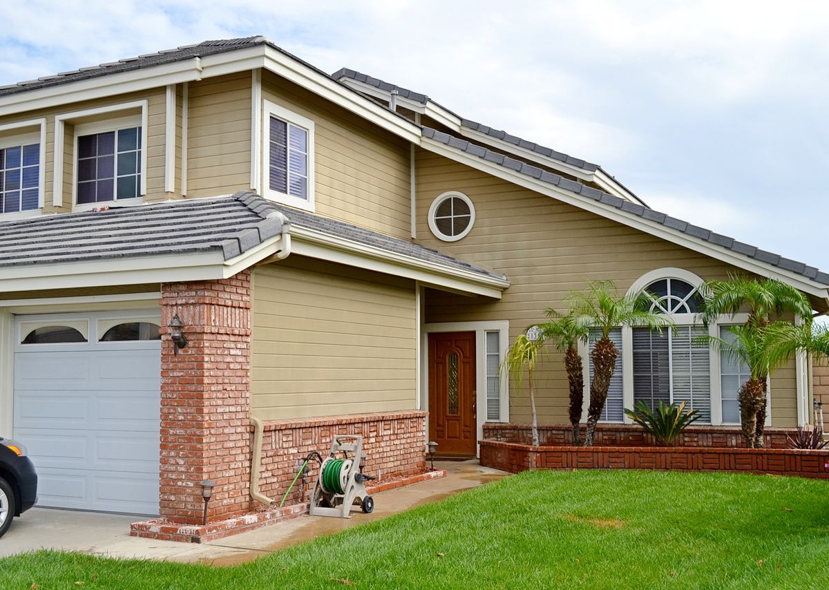 Suburban two-story house with brick and tan siding, white garage door, and a green lawn