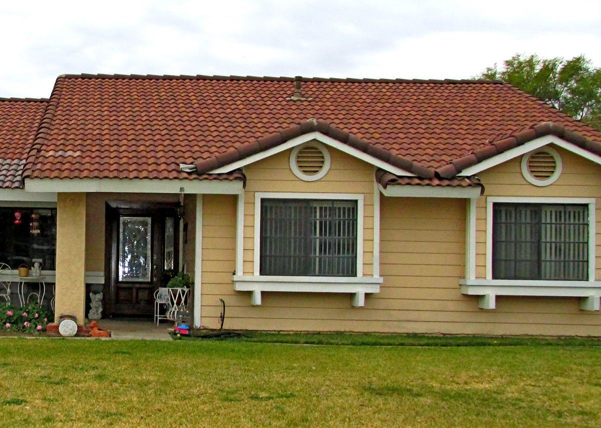 Single-story beige house with red tile roof and white-trimmed windows, front lawn, and covered entryway