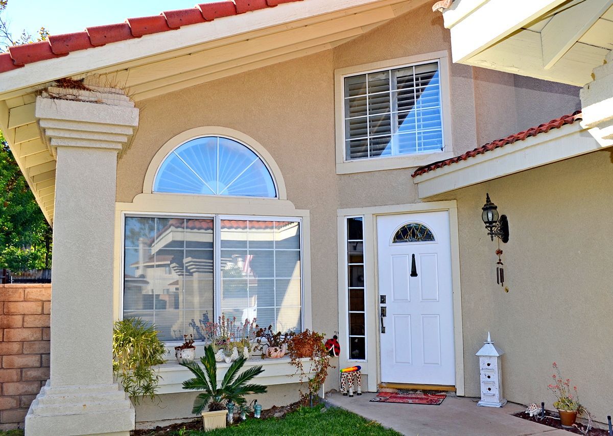 Front exterior of a beige house with a red tile roof, white door, and large arched window.