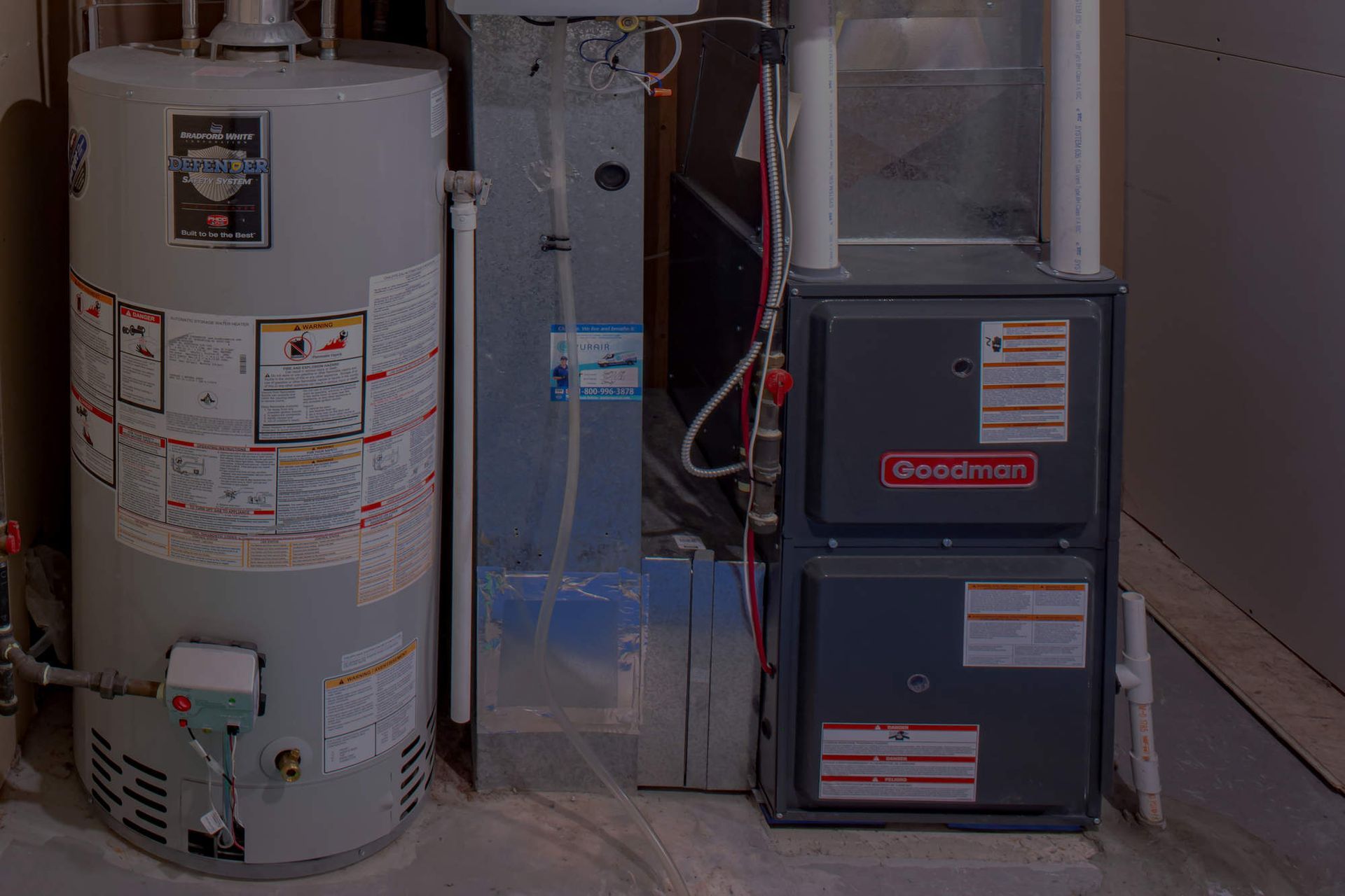 Water heater and furnace units in a utility closet with exposed pipes and ductwork.