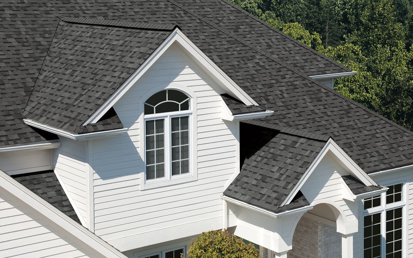 White house roof with dark shingles and dormer windows surrounded by trees