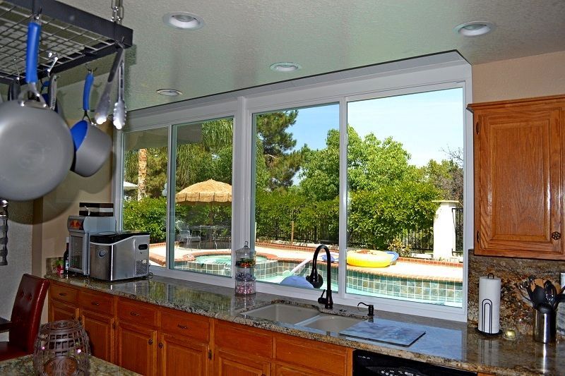 Kitchen sink overlooking a sunny backyard pool, with wooden cabinets and hanging pots and pans.