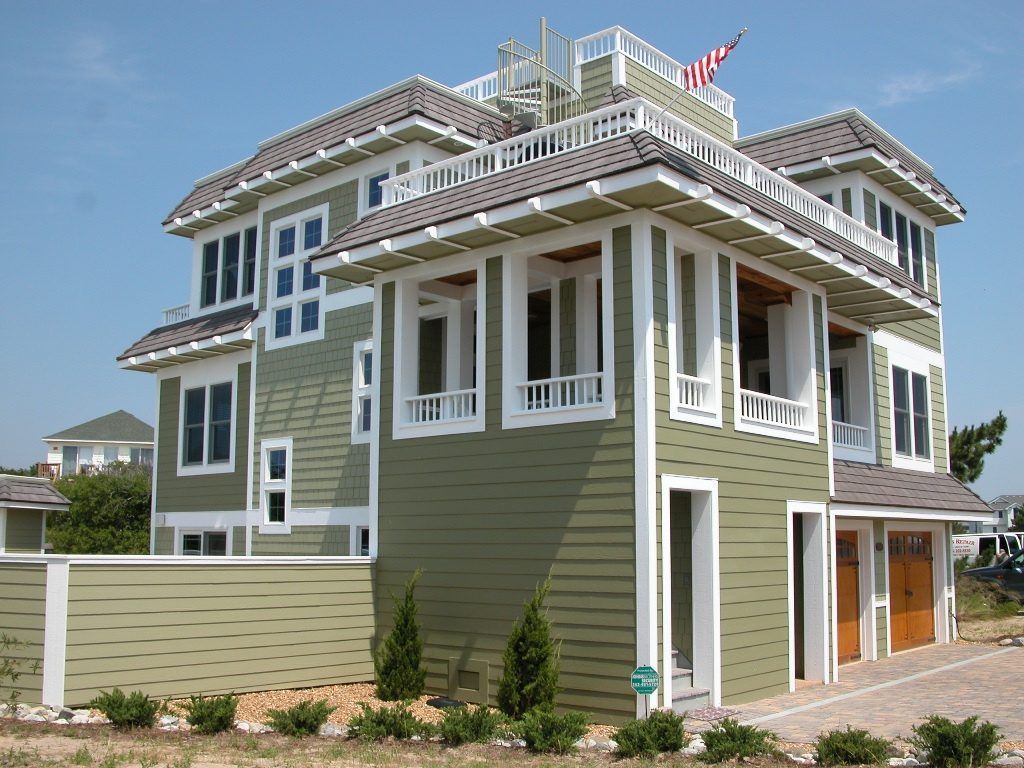 Green two-story coastal house with white trim and balconies beside a paved driveway
