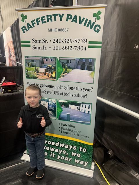 A young child stands in front of a banner for Rafferty Paving, giving two thumbs up.