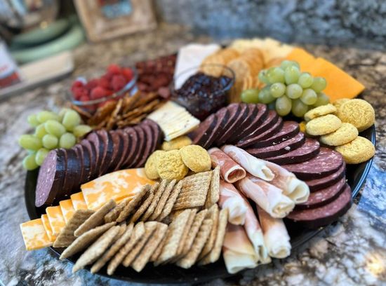 Charcuterie board with cheese, crackers, meats, grapes, raspberries, and jam.