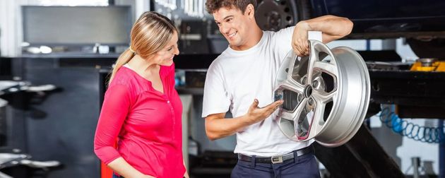 Two people examining a car wheel in a mechanic's garage, one holding the rim and pointing at it