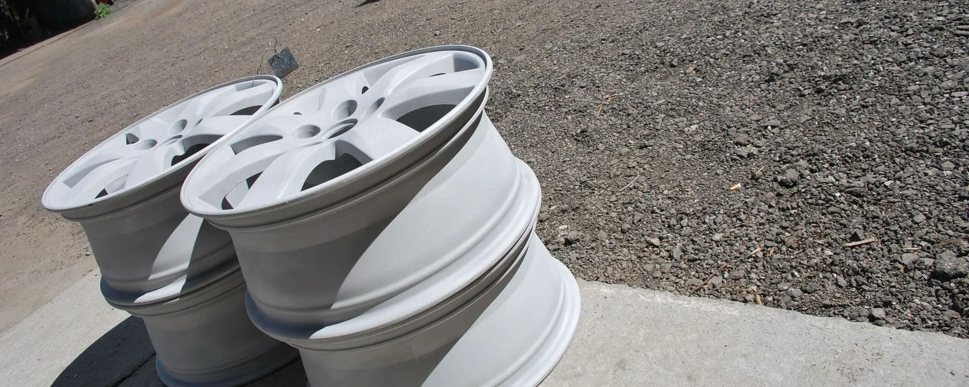 Stacked white car rims on a concrete curb beside gravel ground