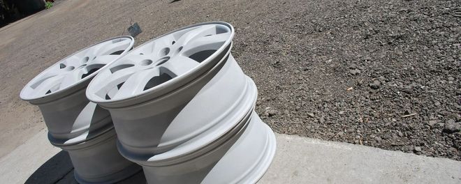 Stacked white car rims on a concrete curb beside gravel ground