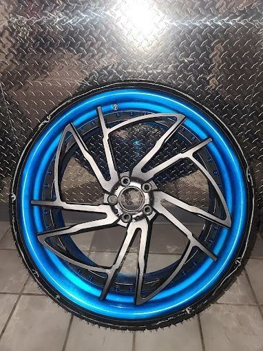 Blue-rimmed motorcycle wheel with a black-and-silver spoked rim on a diamond-plate background
