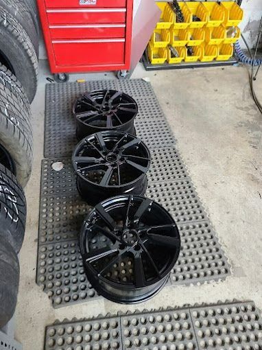 Three black car rims on a workshop mat beside a red tool chest and yellow parts bins