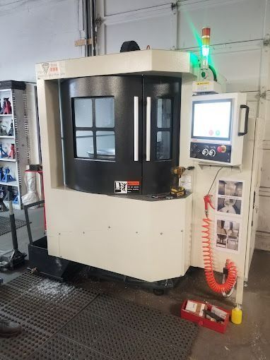 Industrial CNC machine with a control panel in a workshop, black and beige enclosure, red coiled hose nearby