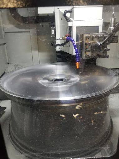 CNC machine cutting a large metal disk with a coolant nozzle in a workshop