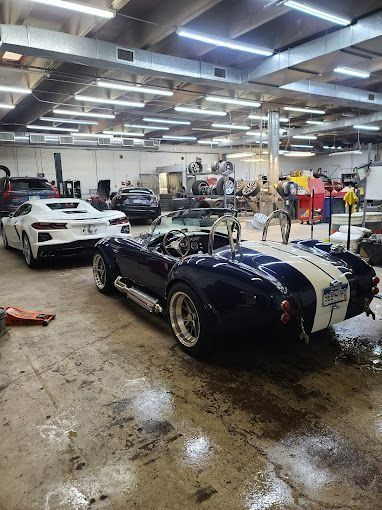 Classic sports cars in a garage, including a blue-and-white roadster and a white coupe on a wet floor.