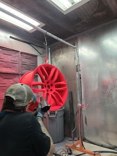 Person spray-painting a bright red wheel rim in a workshop booth