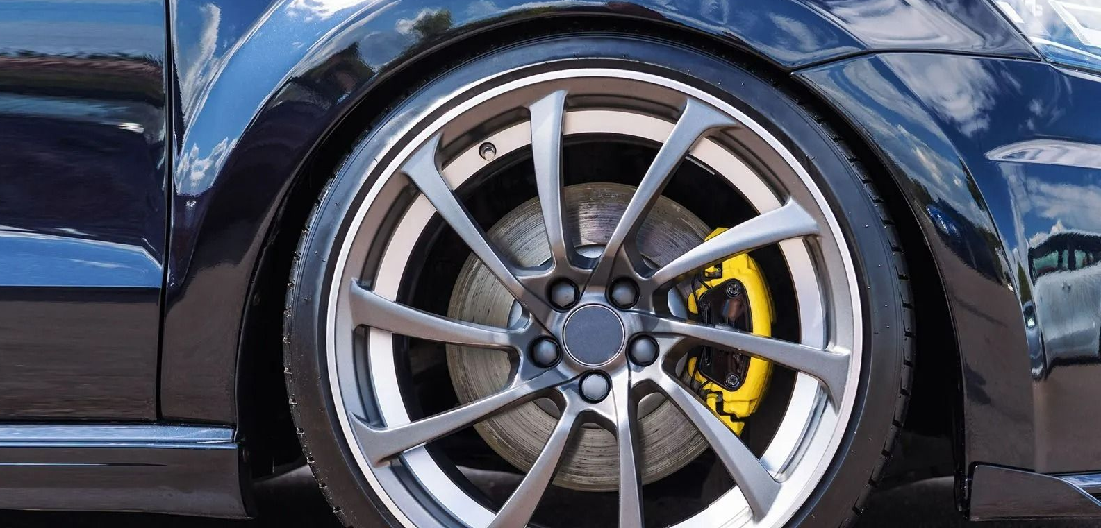 Close-up of a blue sports car&rsquo;s silver alloy wheel with a yellow brake caliper