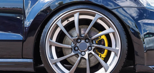 Close-up of a blue sports car&rsquo;s silver alloy wheel with a yellow brake caliper