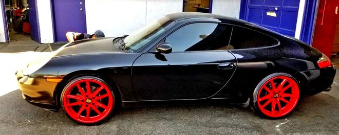 Black sports coupe with bright red wheels parked outdoors