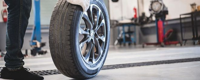Car tire being checked in an auto repair shop, with a mechanic standing nearby.