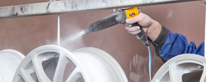 Person spray-painting white car rims in a workshop using a handheld spray gun