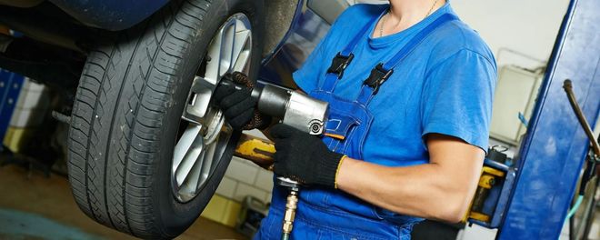 Mechanic using a power tool to remove a car tire in an auto shop