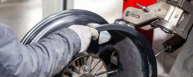 Gloved worker fitting a black tire onto a wheel in a workshop