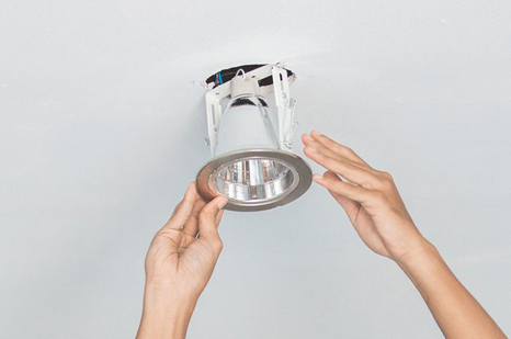 A person is installing a light fixture in a ceiling