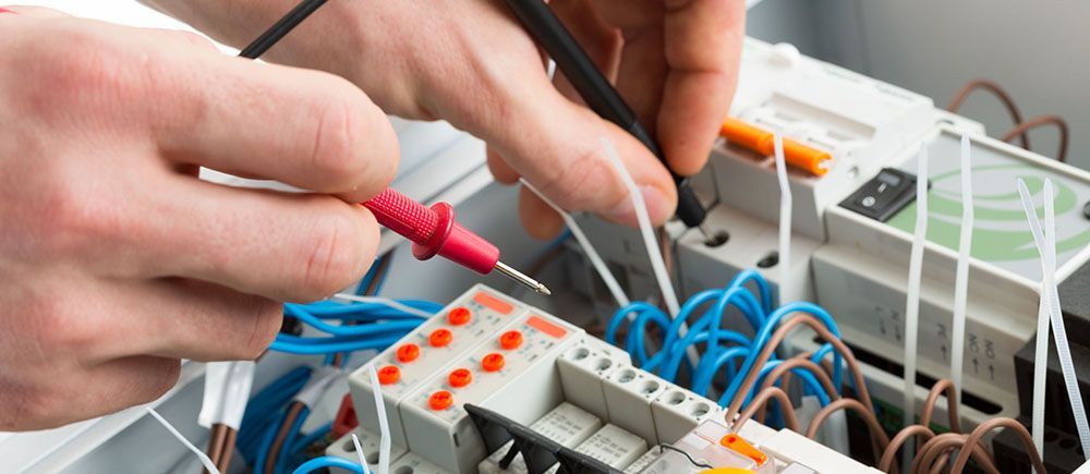 An electrician is working on an electrical box with a multimeter