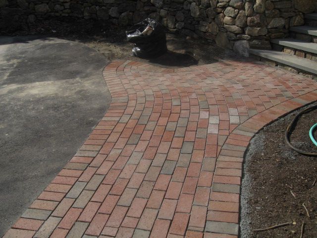 A brick walkway with a green hose on the side
