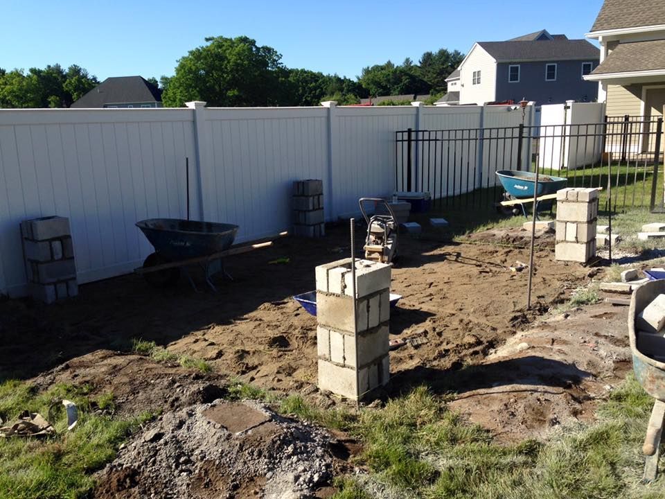 A backyard with a white fence and bricks in the dirt