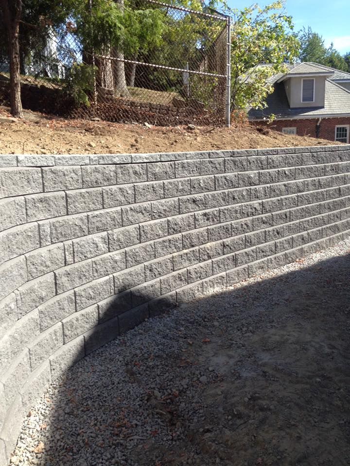 A brick wall is sitting on top of a dirt hill next to a house.