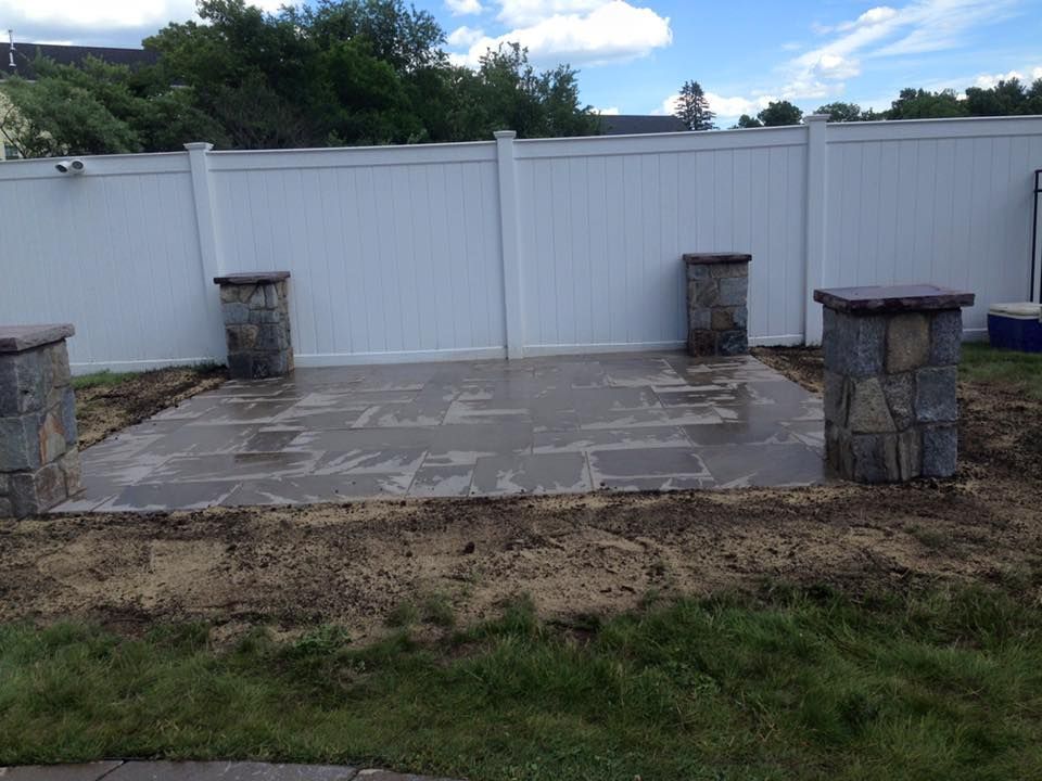 A backyard with a white fence and a stone patio.
