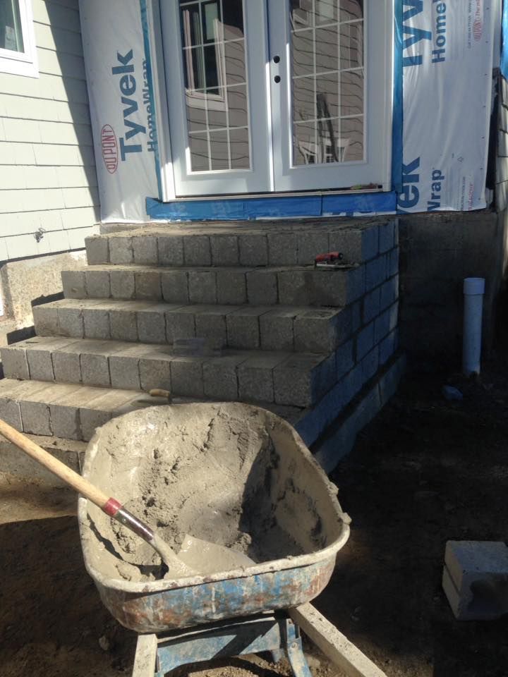 A wheelbarrow is filled with cement next to a set of stairs