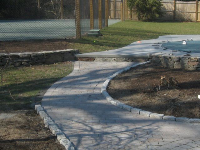 A walkway leading to a pool with a tennis court in the background