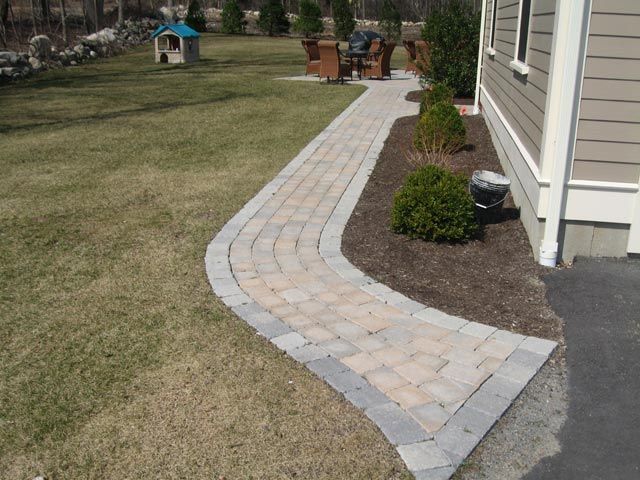 A brick walkway leading to a house with a dog house in the background