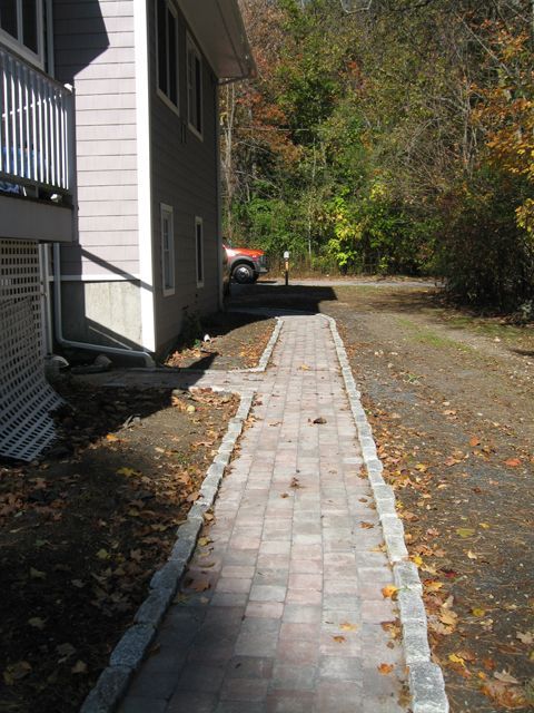 A brick walkway leading to a house with trees in the background