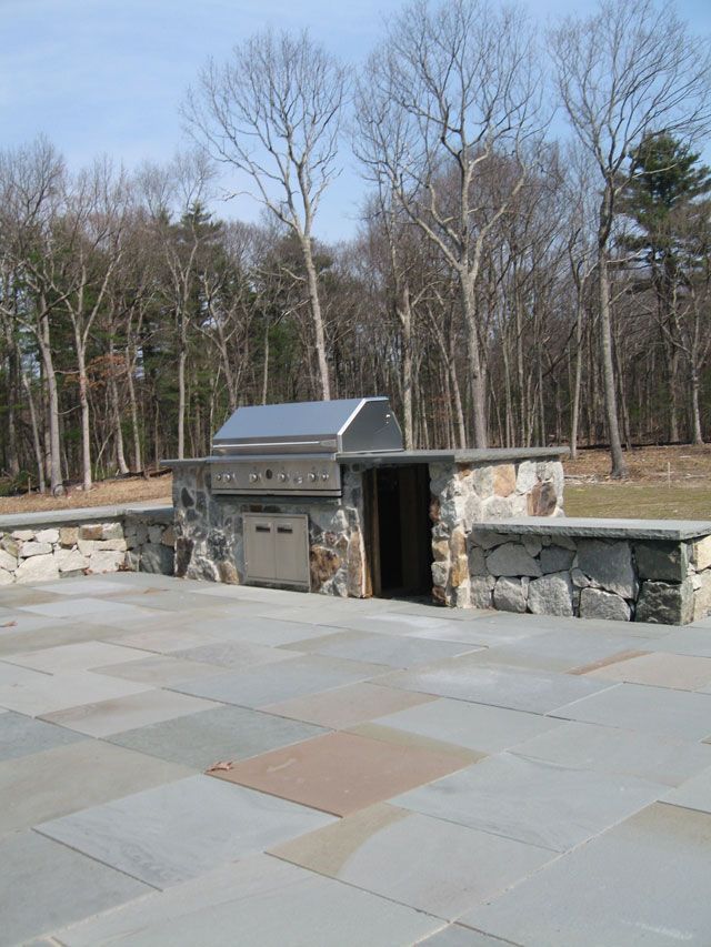 A patio with a grill and trees in the background