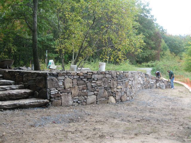 A stone wall is being built in the middle of a dirt field.